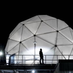 The 38-foot-wide radome protecting the Multi-Band Test Terminal — a large antenna on an MIT Lincoln Laboratory building rooftop — is shown illuminated at night.